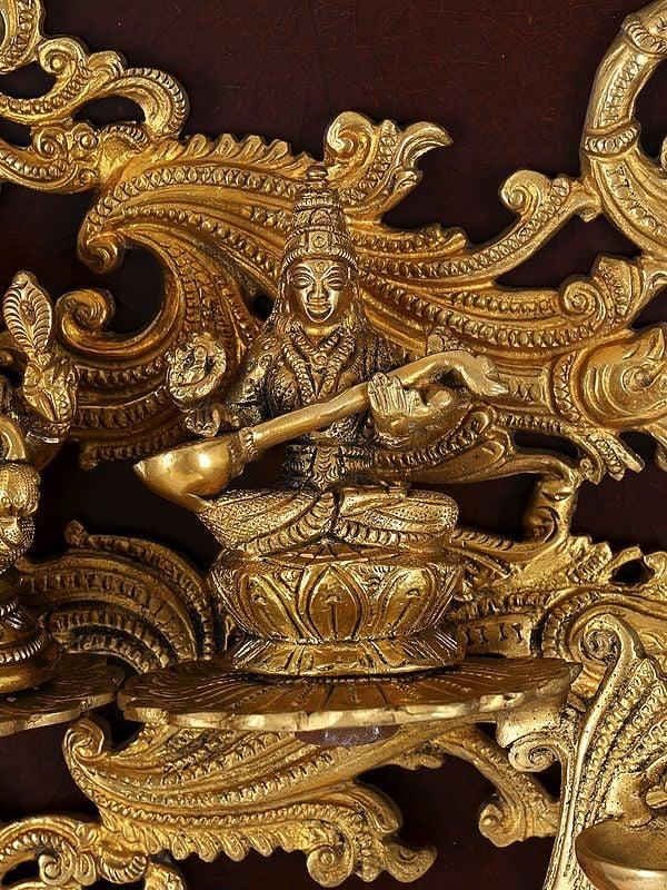 Exotic India 24" Lakshmi Ganesha Saraswati With Diya | Wood Framed Brass Sculpture | Wall Hanging 